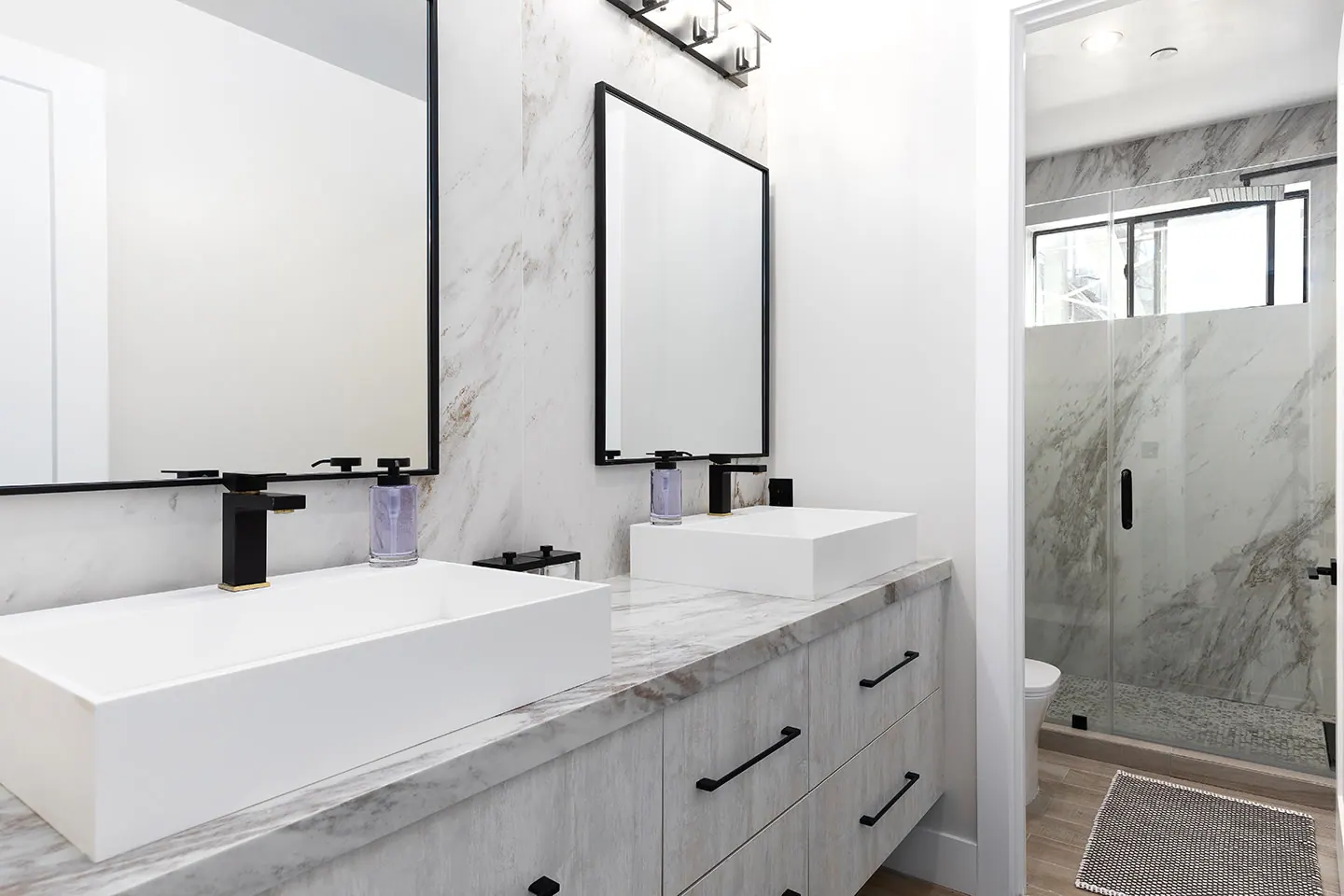 Light bathroom with marble finishes, twin sinks and black-framed mirrors